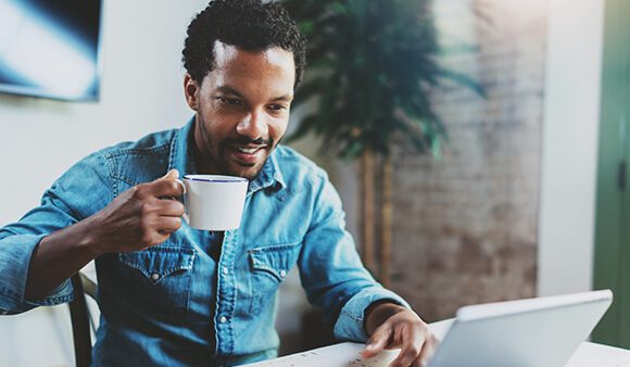 man drinking coffee and typing on computer