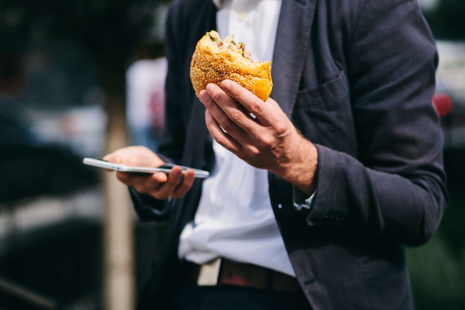 man with burger in one hand, phone in the other