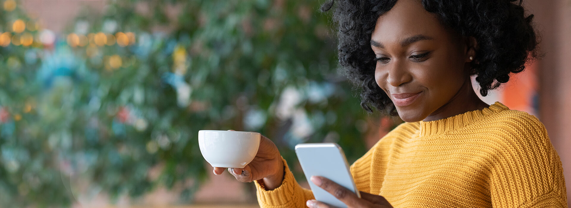 woman smiling at her phone with coffee in her hand