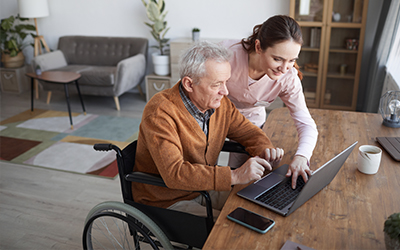 man in wheelchair on laptop guided by woman