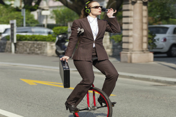 woman with headphones on riding unicycle drinking coffee