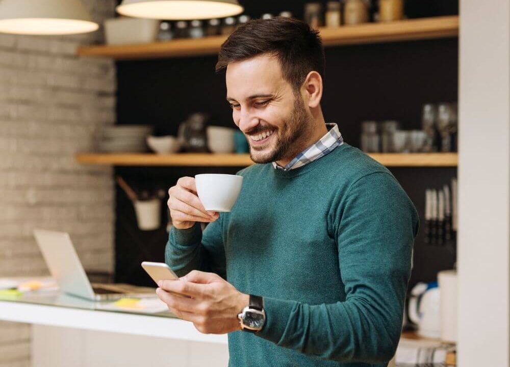 man smiling at phone with coffee