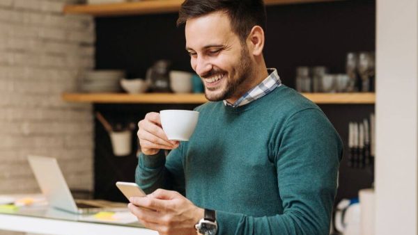 man smiling at phone with coffee