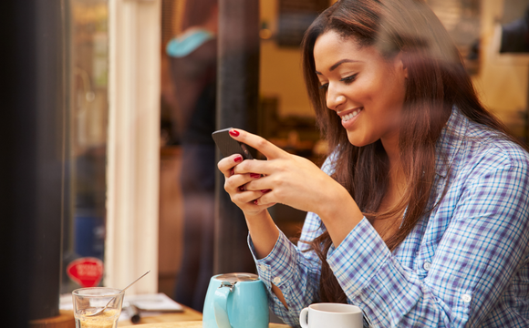 woman sat with coffee smiling at phone