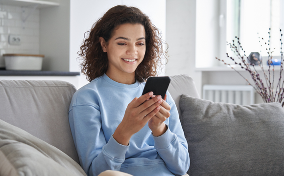 woman sat on sofa smiling at phone