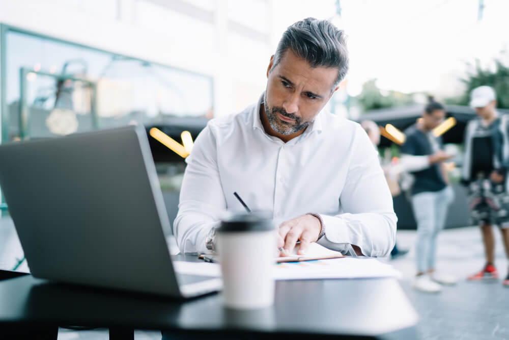 man writing while looking at laptop