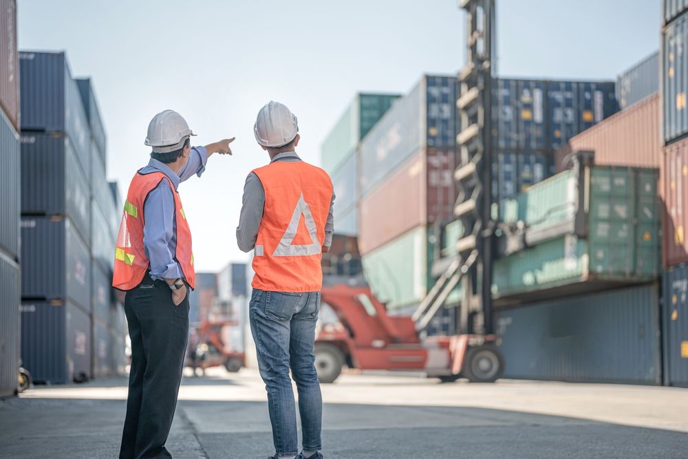 two men in PPE pointing towards containers