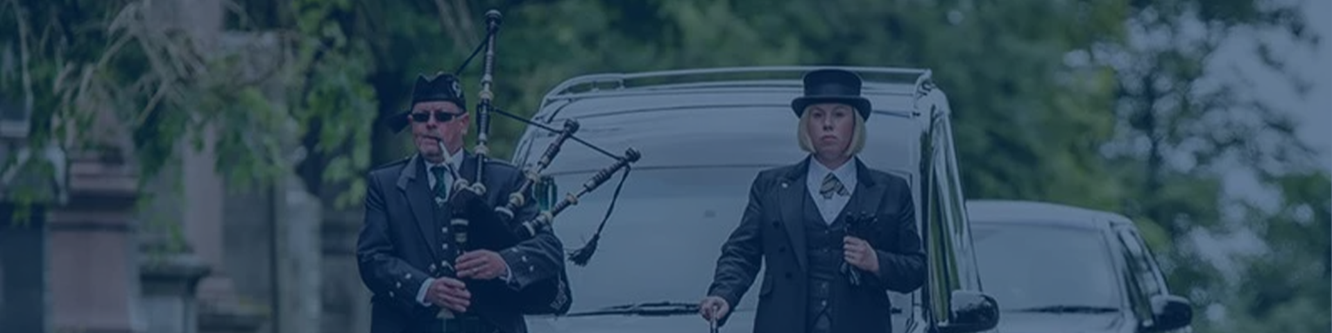 funeral procession led by woman and man playing bagpipes