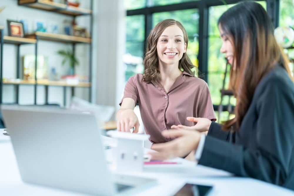 two women smiling at each other sat at laptop