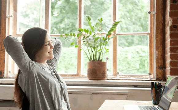 woman smiling at laptop with hands behind head