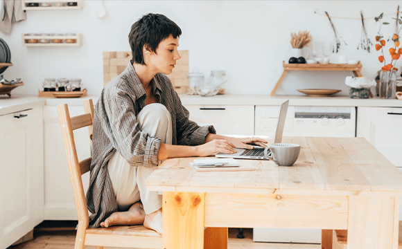 woman sat in kitchen in loungewear on laptop