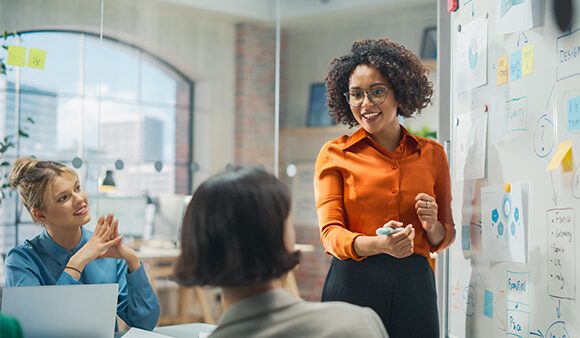 Woman presenting figures on a white board at work to her team.