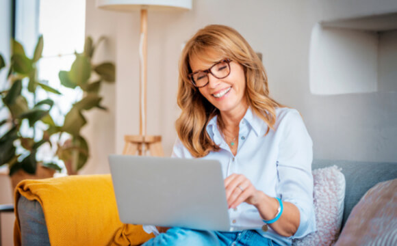 woman sat on sofa smiling at laptop