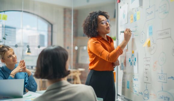 woman writing on whiteboard while colleagues watch