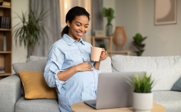 a pregnant woman sat on a sofa smiling at a laptop